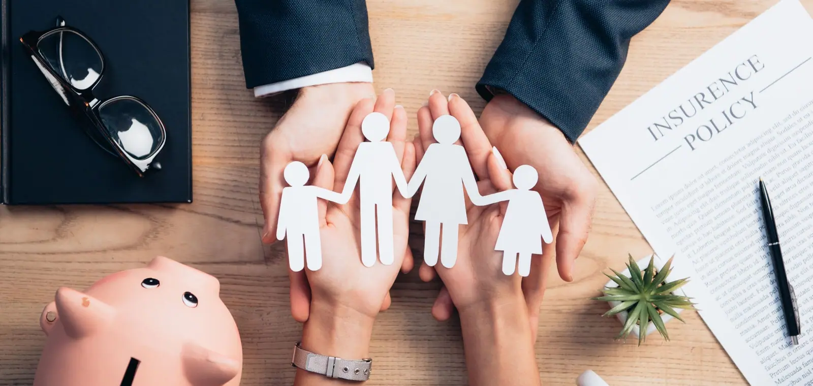 Unas manos junto a una hucha resguardan a una familia de papel, una imagen sobre el precio del seguro de decesos en Algemesí