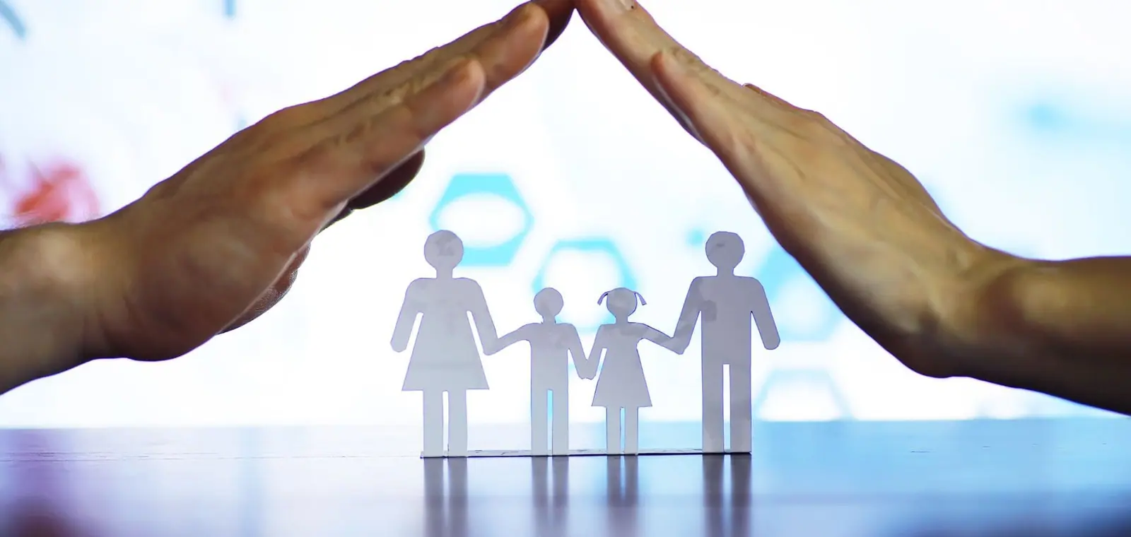 Unas manos que protegen la silueta de papel de una familia, una imagen sobre el precio del seguro de decesos en Ribeira