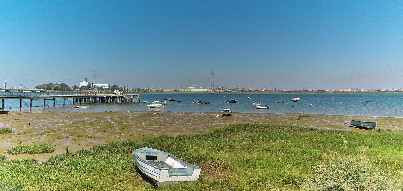 La ría del Tinto en Huelva, con el muelle y las barcas en la orilla, una imagen sobre el precio del seguro de decesos en Huelva